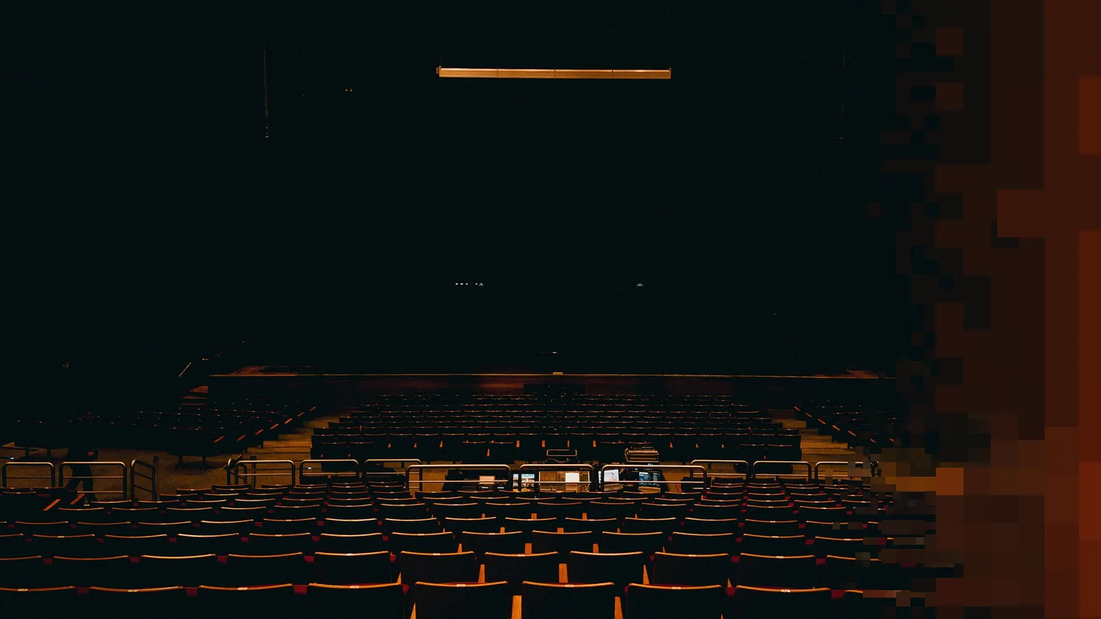 Mørk teatersal med tomme stoler i rader, lysbord midt i salen og en svak lysrigg over scenen