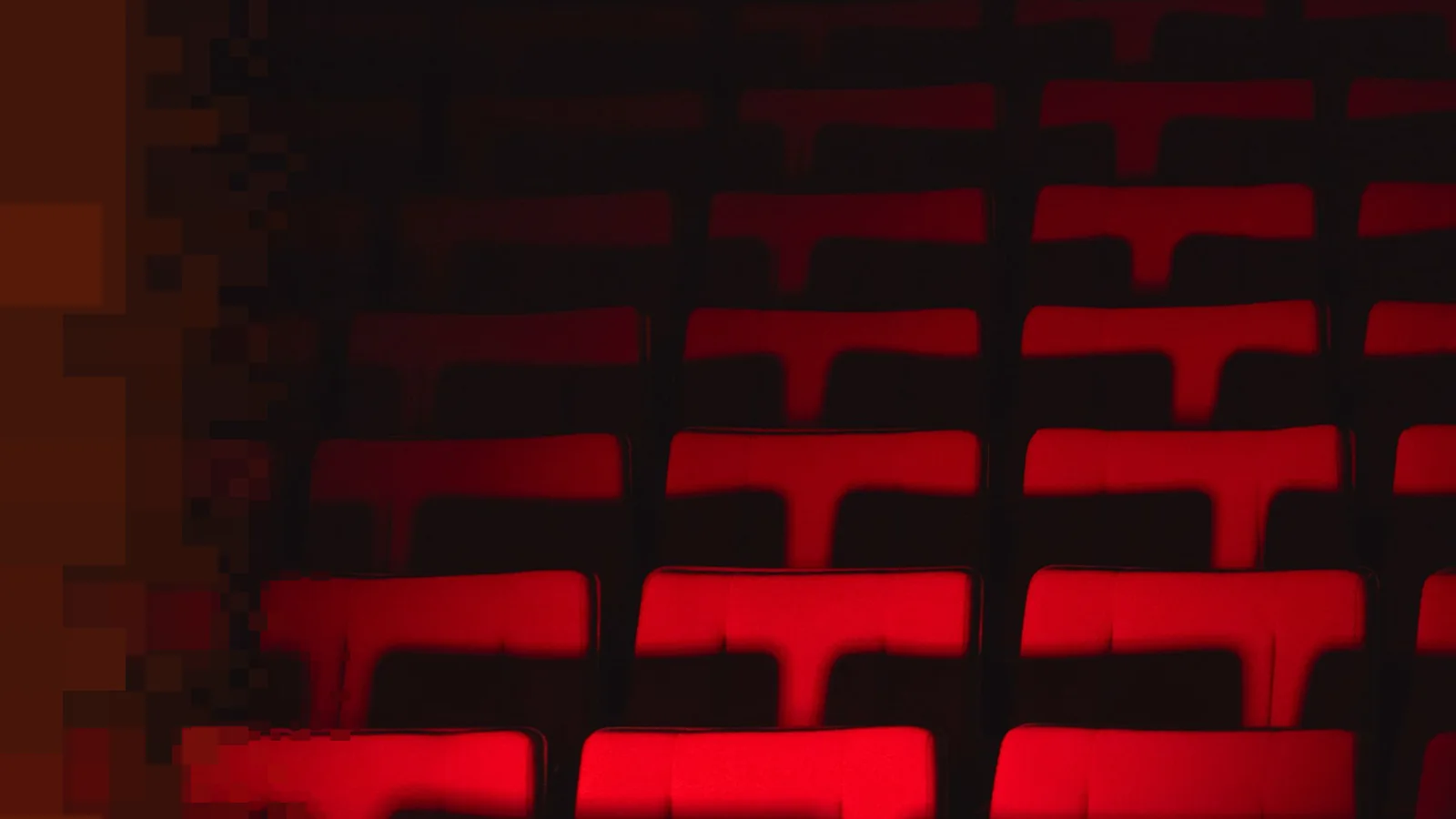 Mørk teatersal med røde seteryggstøtter i rader