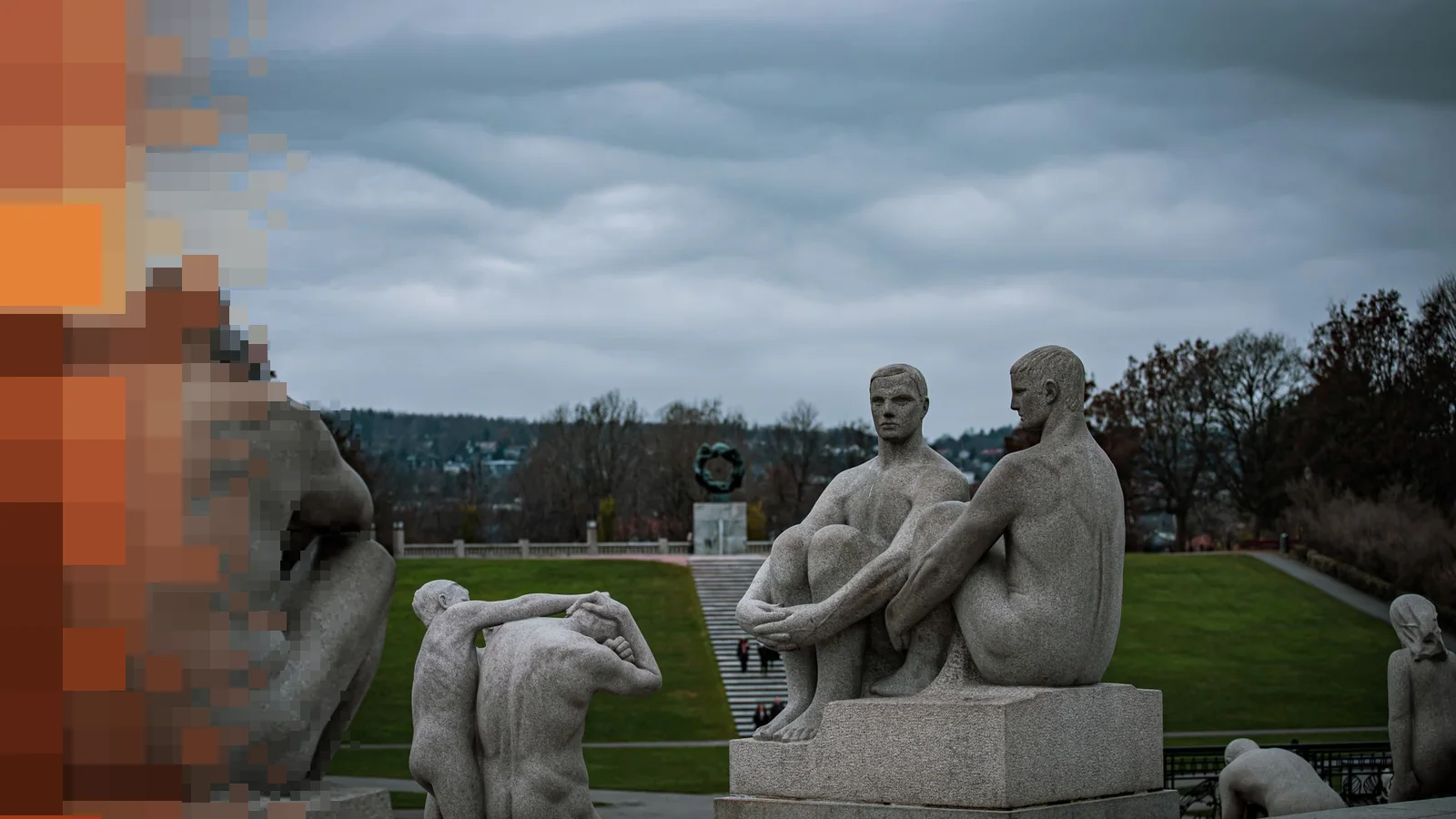 Granittskulpturer av sittende menn i Vigelandsparken en overskyet høstdag, med Livshjulet langt bak