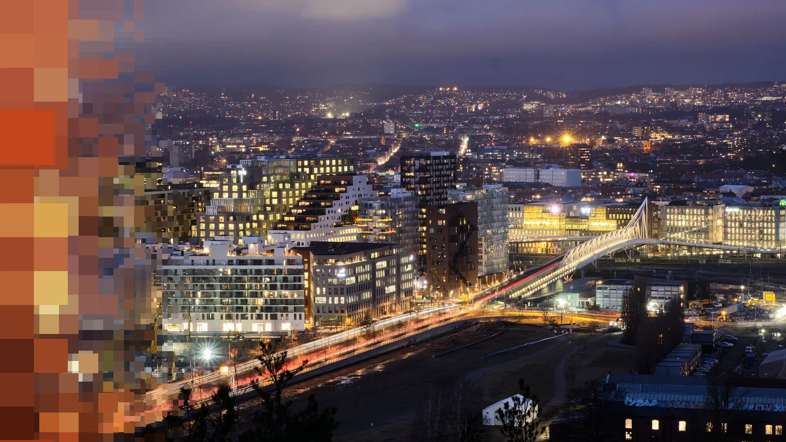 Oslo sett fra Ekeberg en vinterkveld, med opplyste høyhus i Barcode, lysspor fra trafikken og en hvit gangbro over sporene