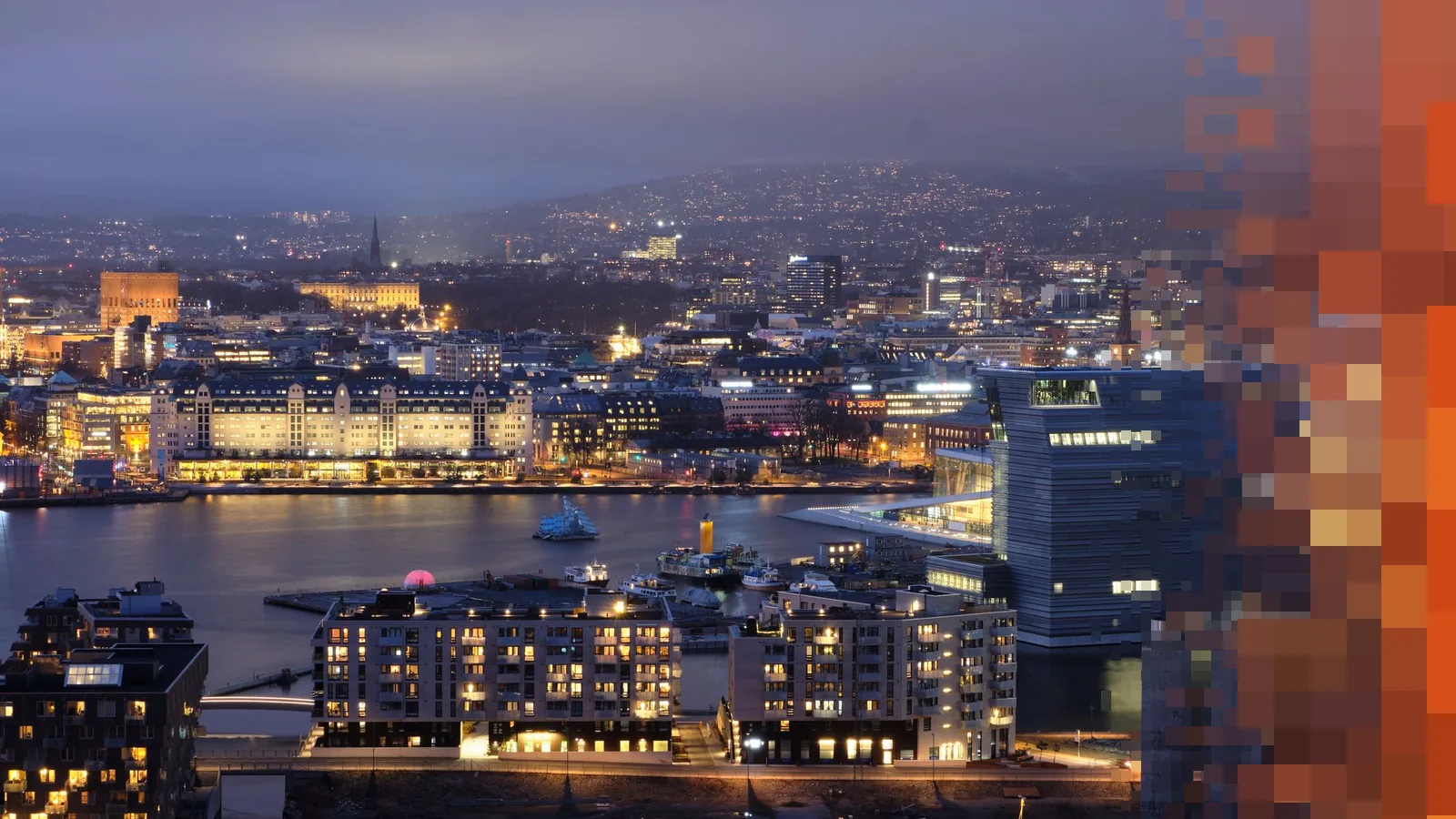 Oslo sentrum i blåtimen sett ovenfra, med lys i husene langs havnen og åsene bak byen