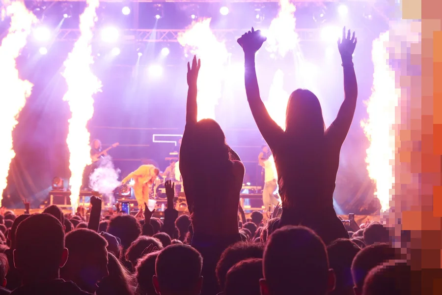 Publikum med armene i været foran en festivalscene der store flammesøyler skyter opp i lilla lys