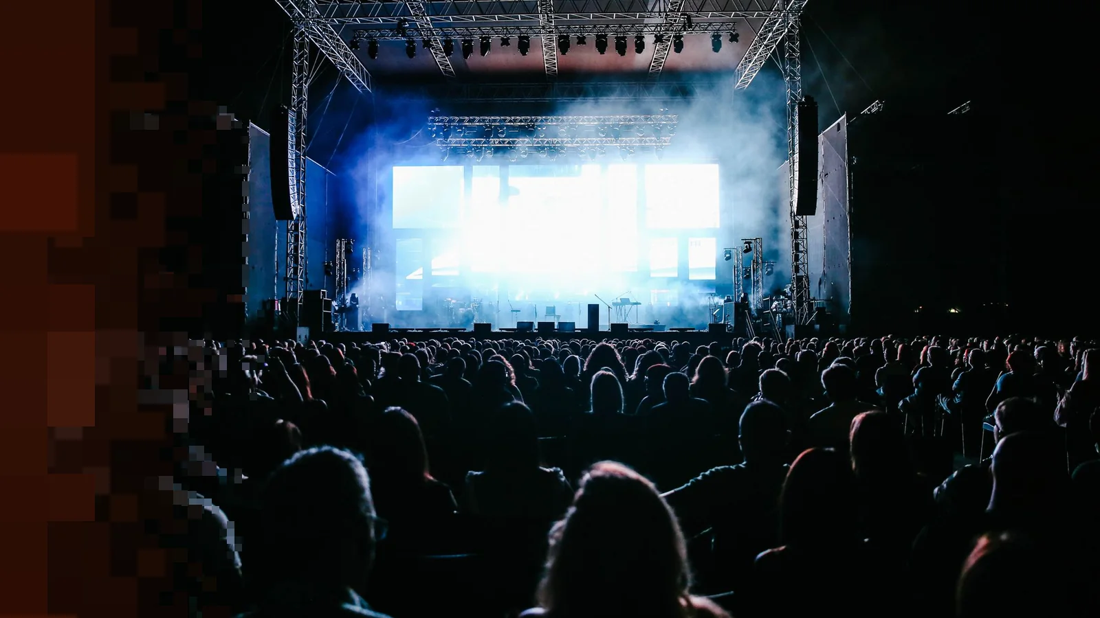 Stor konsertscene med røykfylt lys og stort publikum fra baksiden i mørket