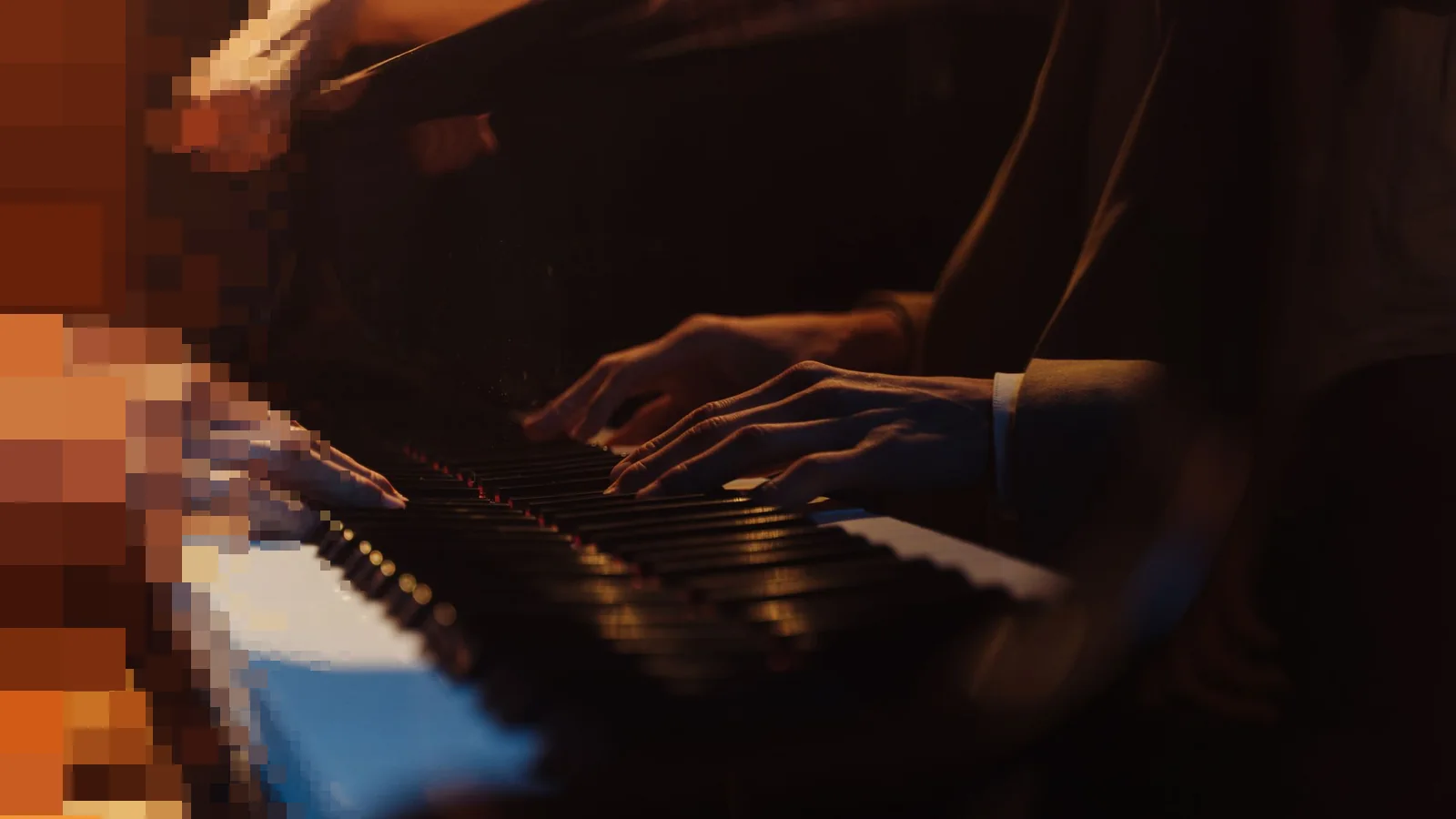 Nærbilde av hender på tangentene til et piano i varmt, dempet lys