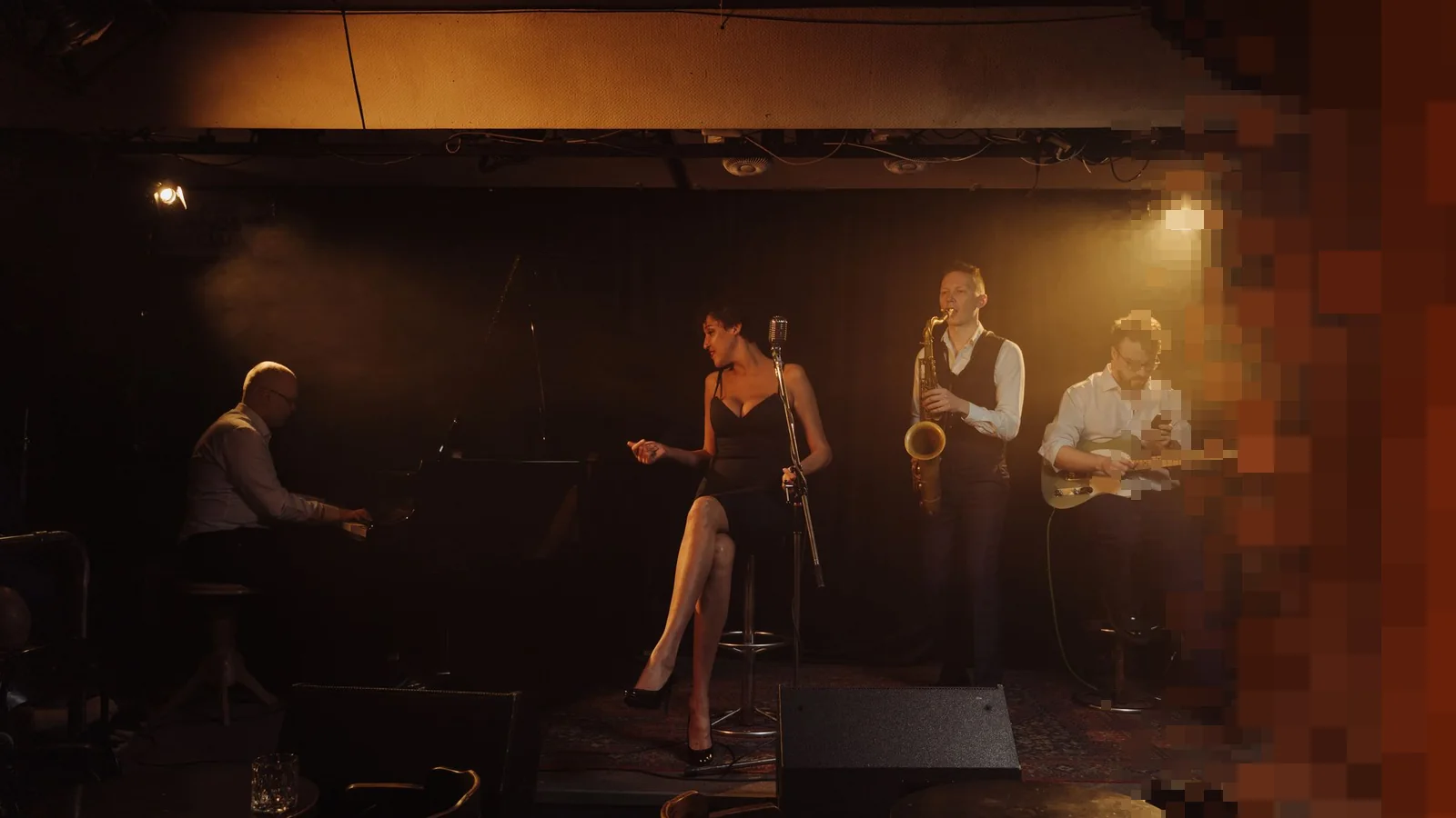 Jazzband med pianist, sangerinne, saksofonist og gitarist på en liten scene i varmt, dempet lys