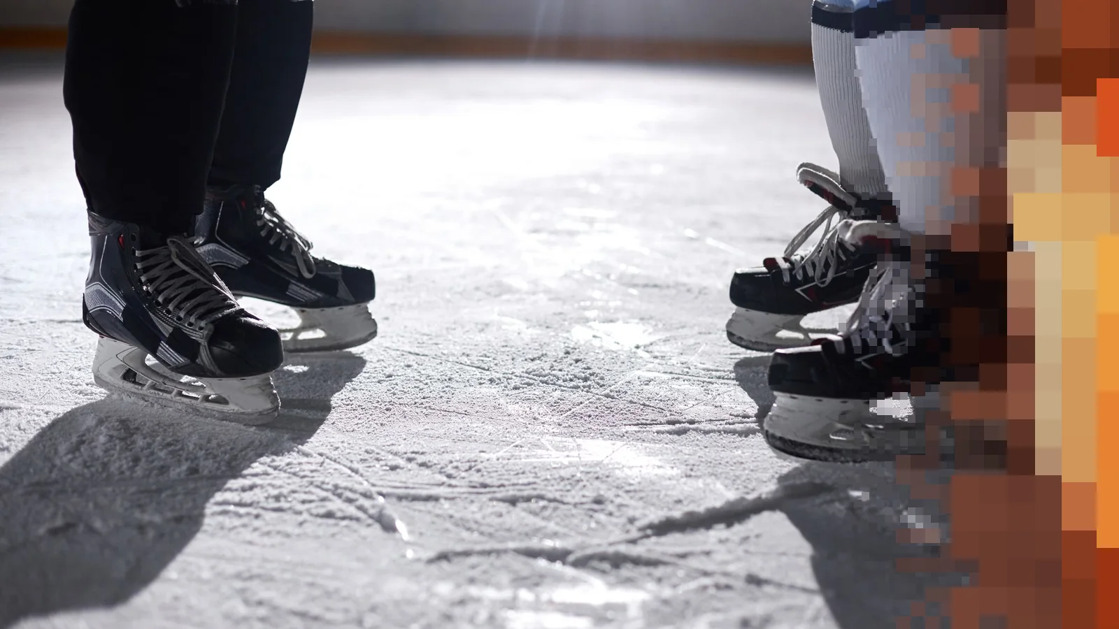 To par svarte hockeyskøyter står vendt mot hverandre på en oppskrapet isflate i skrått sollys